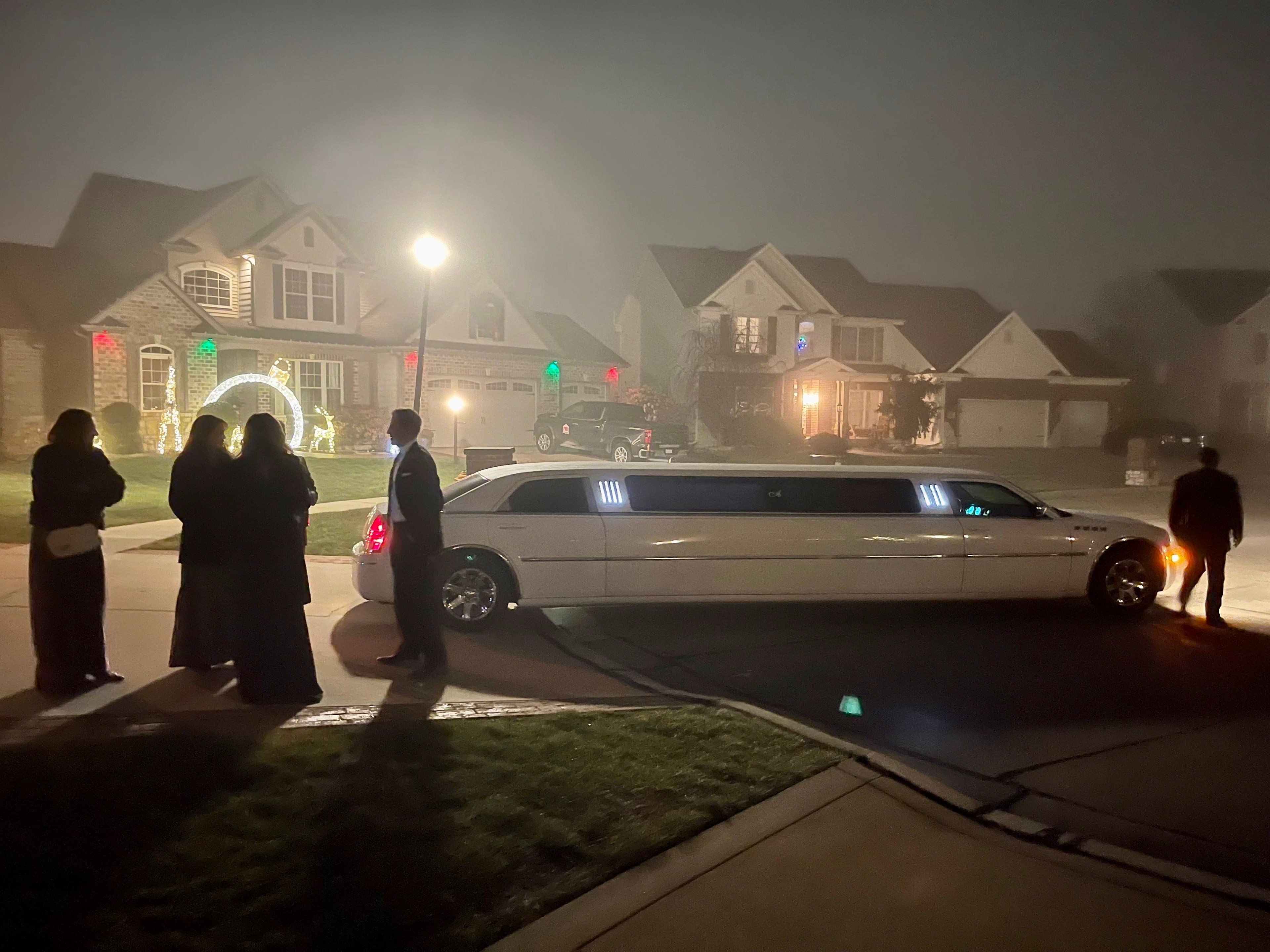 Guests in formal attire arriving by stretch limousine on a foggy evening